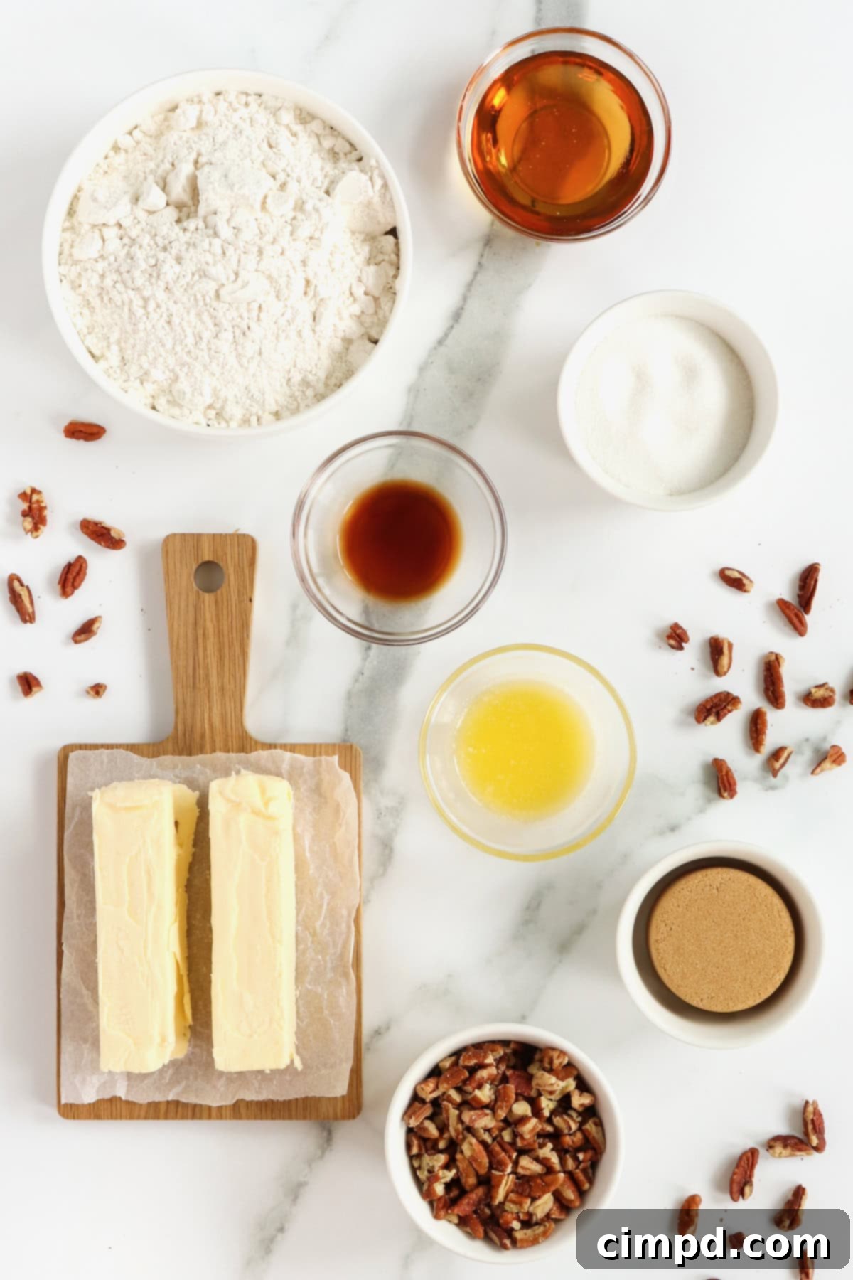 A curated selection of fresh ingredients laid out for making Pecan Pie Thumbprint Cookies on a pristine white marble counter, including butter, sugars, flour, vanilla, and chopped pecans.