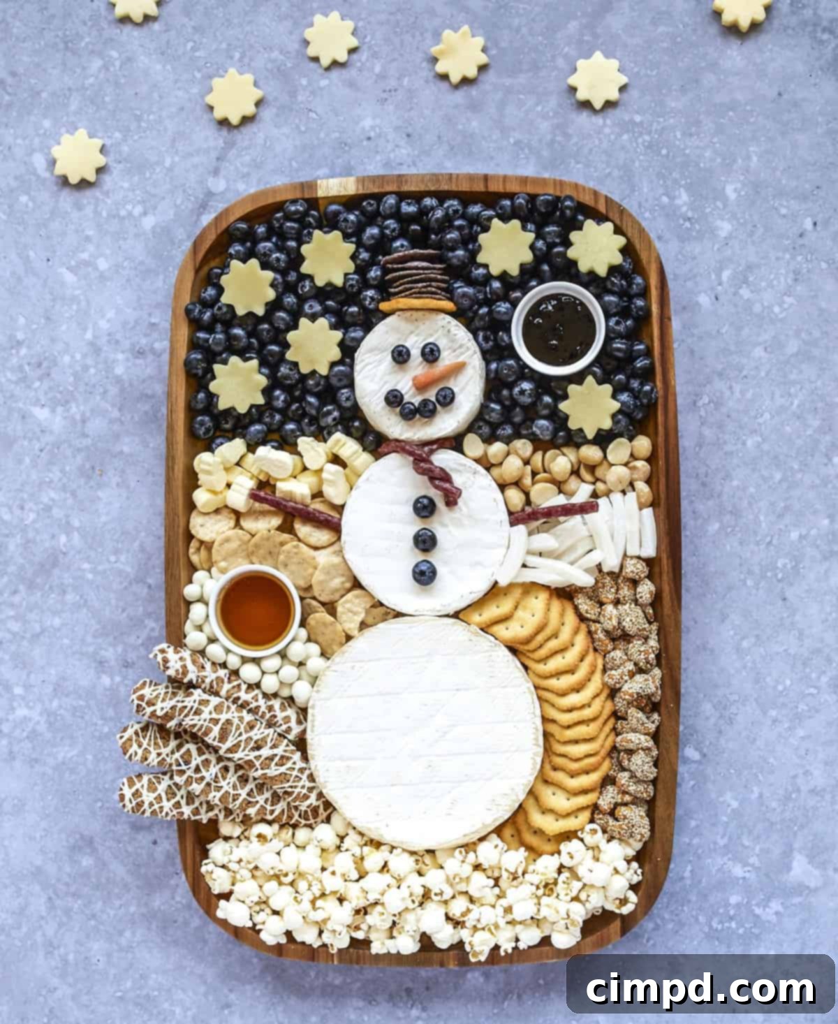 A close-up view of the adorable cheese snowman centerpiece on a rustic wooden board, surrounded by appetizers.