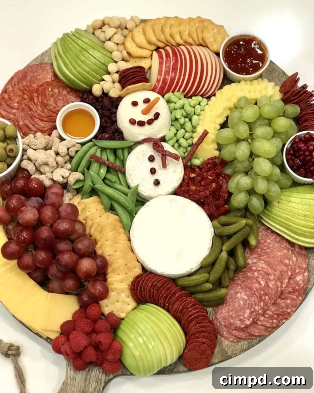 A detailed shot of the cheese snowman's face and body, adorned with pomegranate seeds for features and salami sticks for arms.