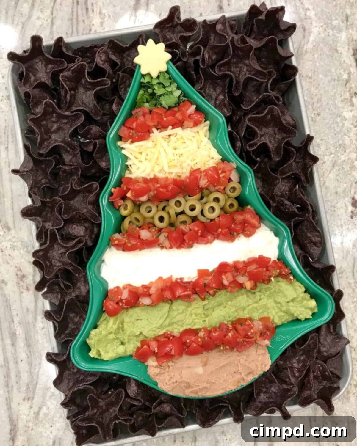 Serving Christmas Tree 7 Layer Dip with tortilla chips by The BakerMama