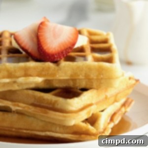A white rimmed plate stacked with three waffles topped with butter and strawberry slices.