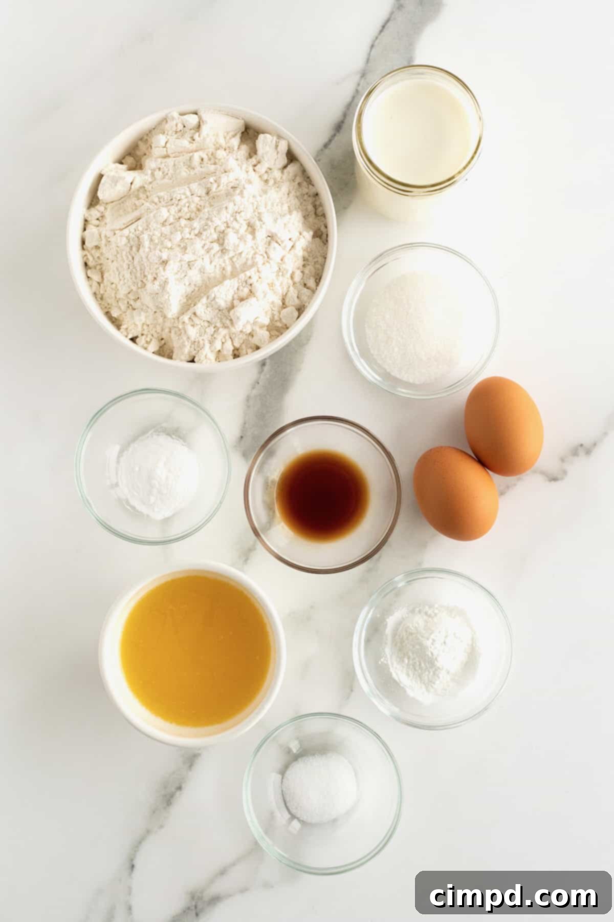Ingredients to make waffles in small glass dishes on a white marble counter.