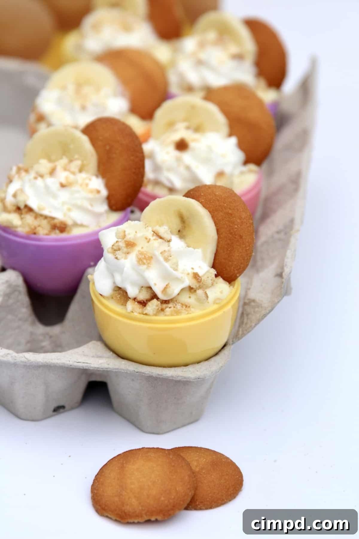 Easter Egg Banana Pudding Cups - a delightful dessert for spring celebrations, featuring layers of vanilla pudding, Nilla wafers, and fresh bananas, presented in colorful plastic egg shells.