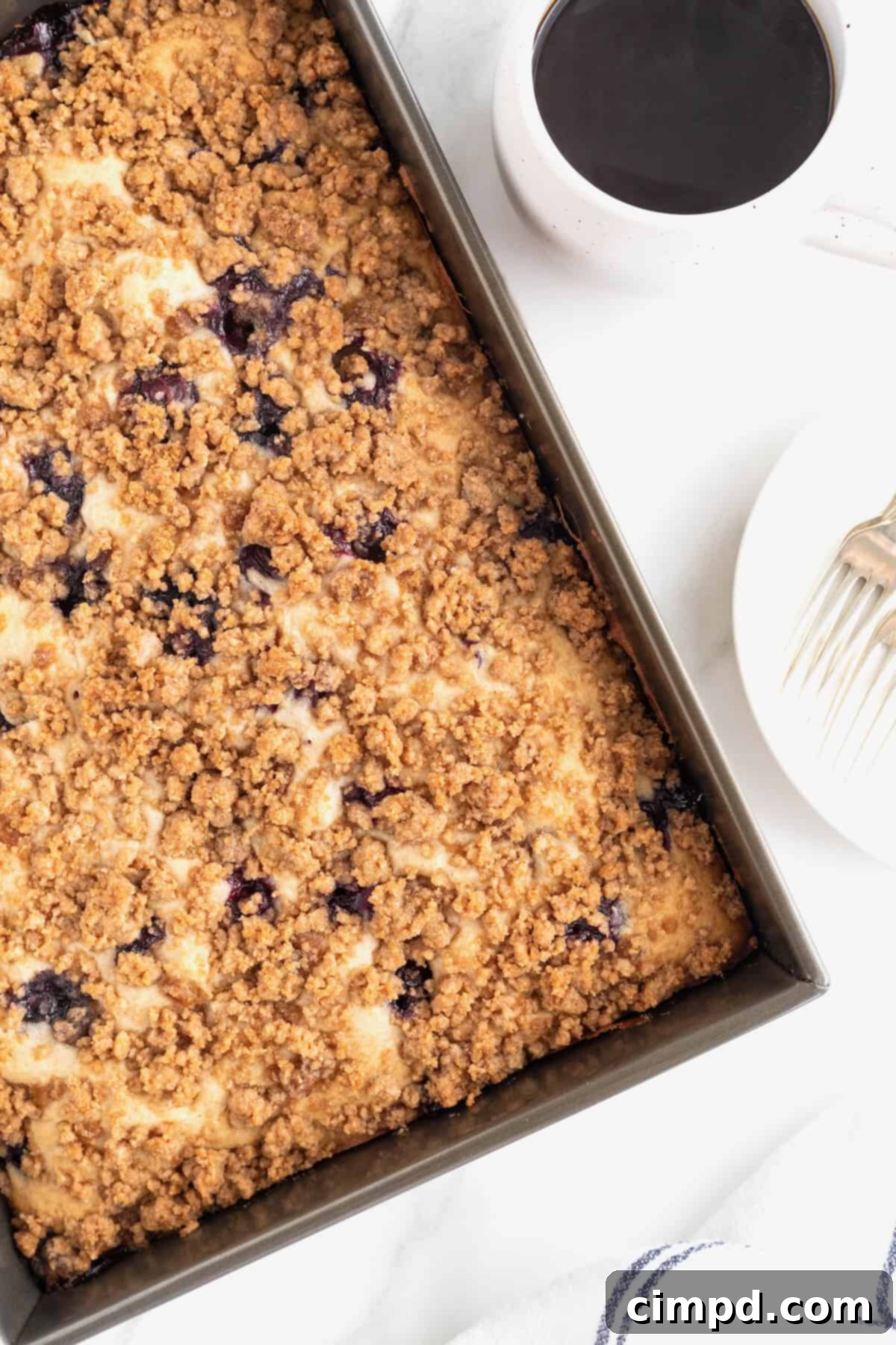 Blueberry Burst Greek Yogurt Crumb Cake 11 A dark baking pan of blueberry coffee cake on a white marble counter.