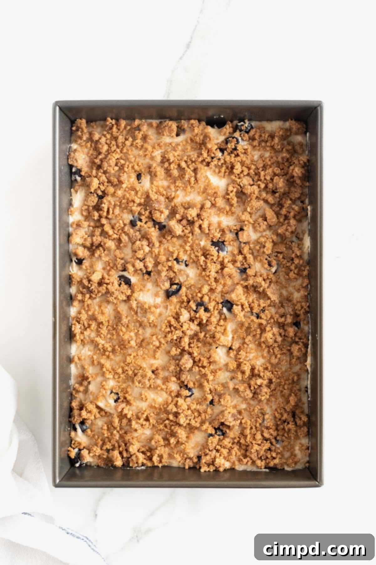 Blueberry Burst Greek Yogurt Crumb Cake 9 A dark baking pan of blueberry coffee cake on a white marble counter.