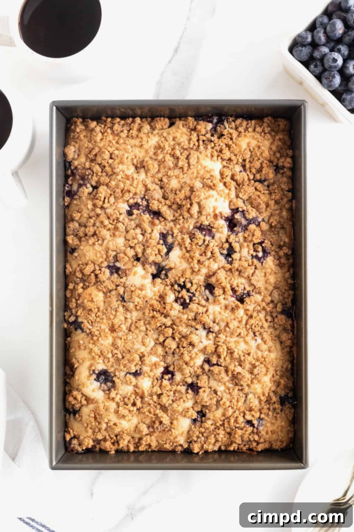 Blueberry Burst Greek Yogurt Crumb Cake 10 A dark baking pan of blueberry coffee cake on a white marble counter.