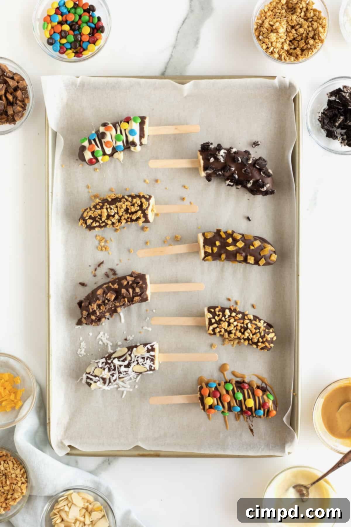 Frozen bananas with popsicle sticks covered in chocolate and mini M&Ms, mini chocolate chips, crushed peanuts and coconut.