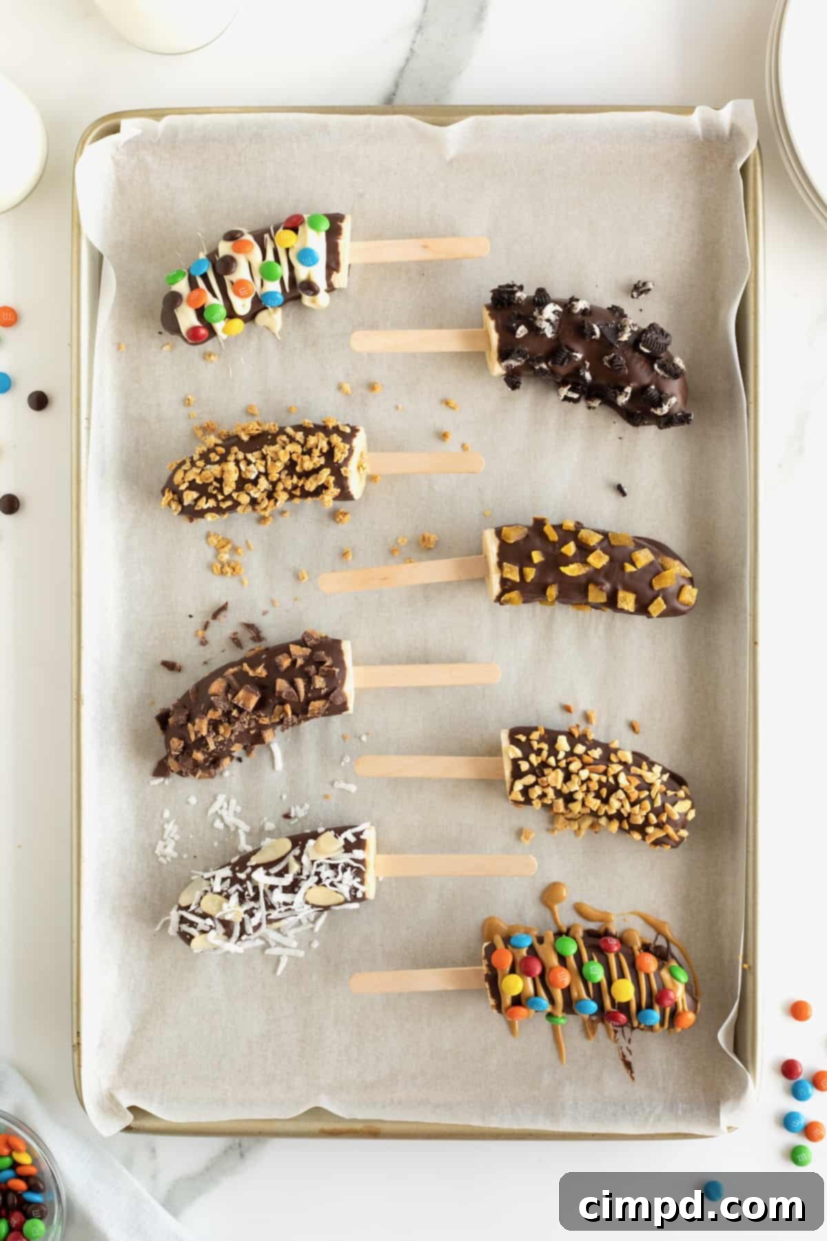 Frozen bananas with popsicle sticks covered in chocolate and mini M&Ms, mini chocolate chips, crushed peanuts and coconut.