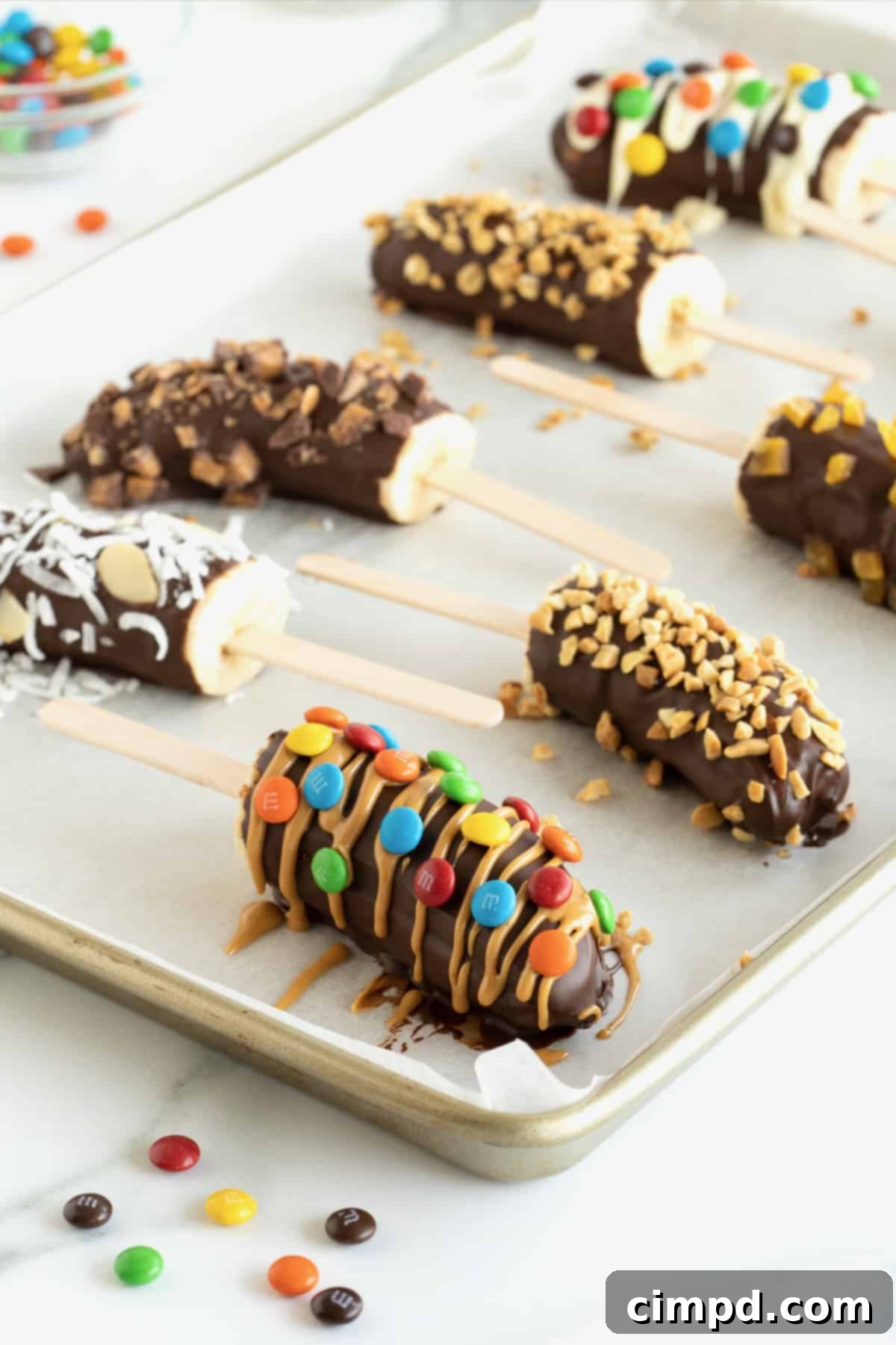 Frozen bananas with popsicle sticks covered in chocolate and mini M&Ms, mini chocolate chips, crushed peanuts and coconut.