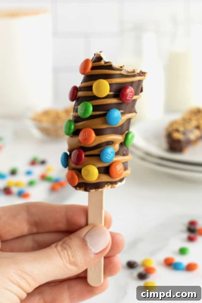 A frozen banana on a popsicle stick, dipped in chocolate, coated in M&Ms and drizzled with melted peanut butter.