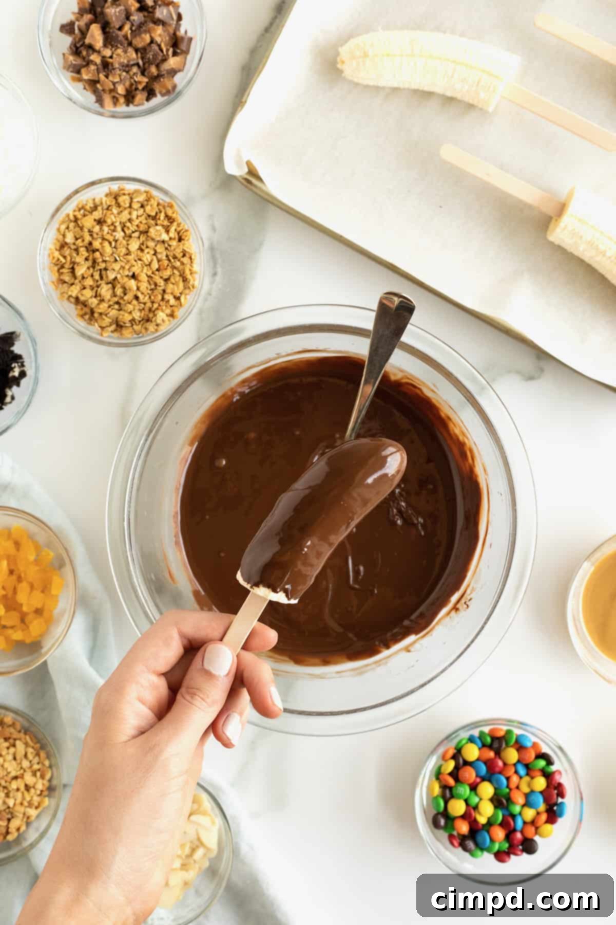 A banana on a popsicle stick being dipped into melted chocolate. 