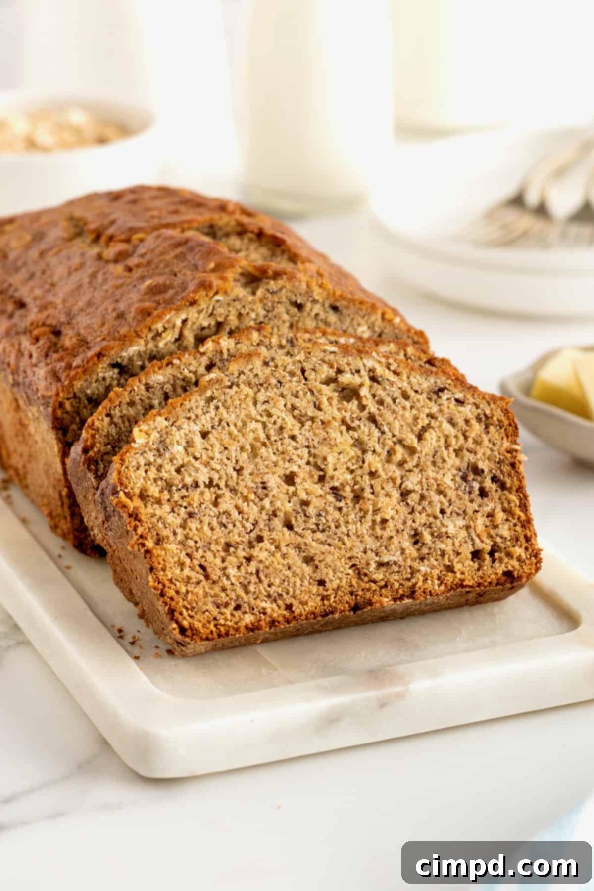 Banana Oat Whole Wheat Bread 10 A loaf of banana bread with two slices cut from it on a white marble bread board.