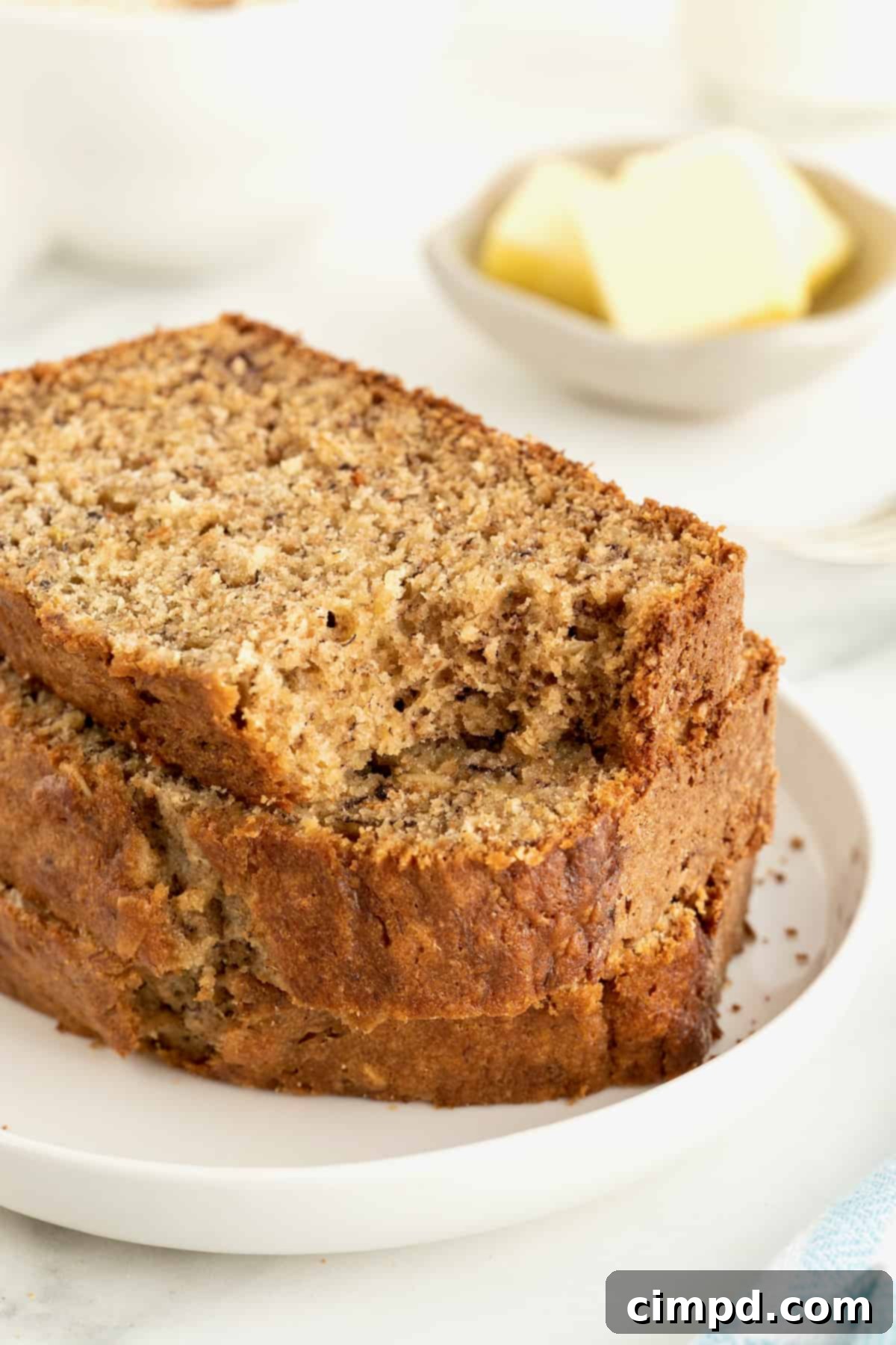 Banana Oat Whole Wheat Bread 3 A stack of three slices of whole wheat banana bread on a white rimmed plate. The top slice has a bite taken out of it.