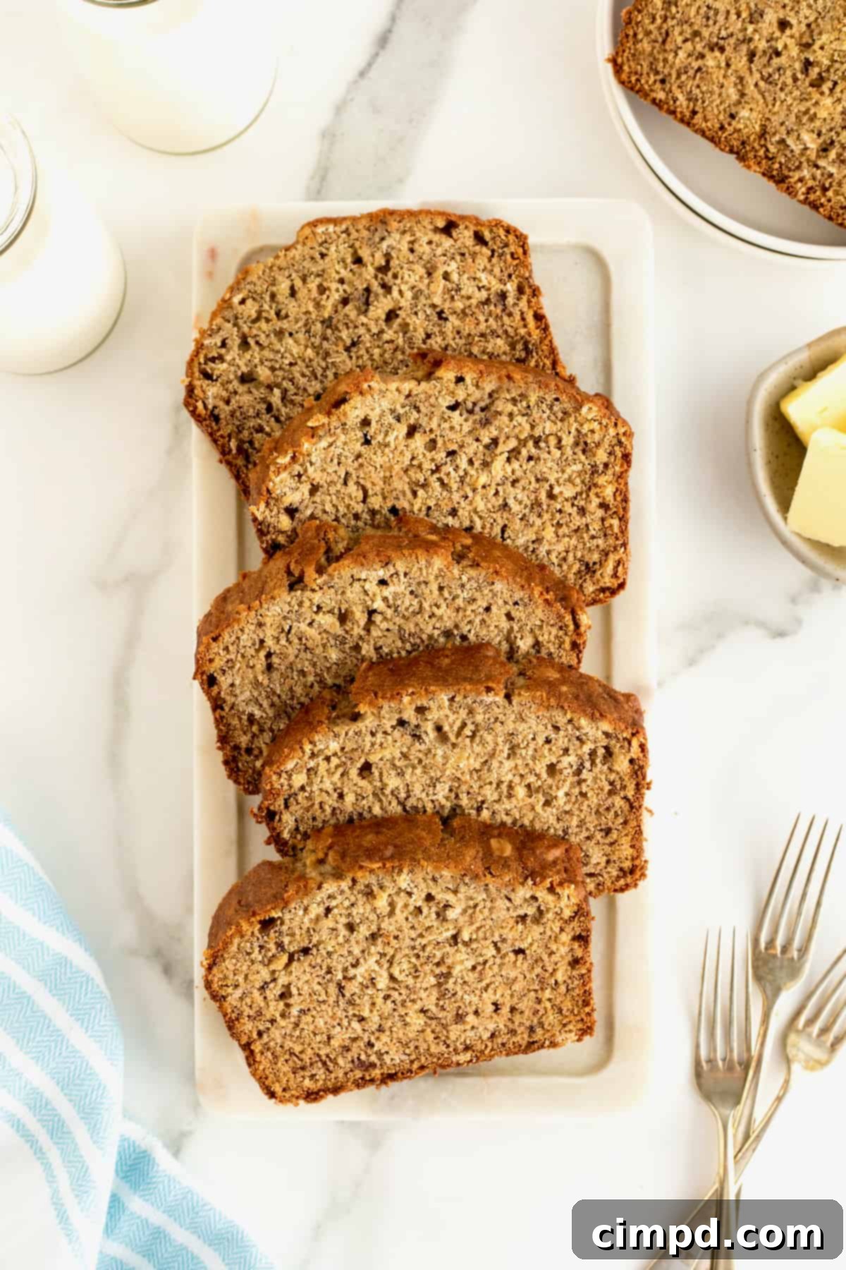 Banana Oat Whole Wheat Bread 4 A sliced loaf of banana bread arranged on a. white marble bread board.