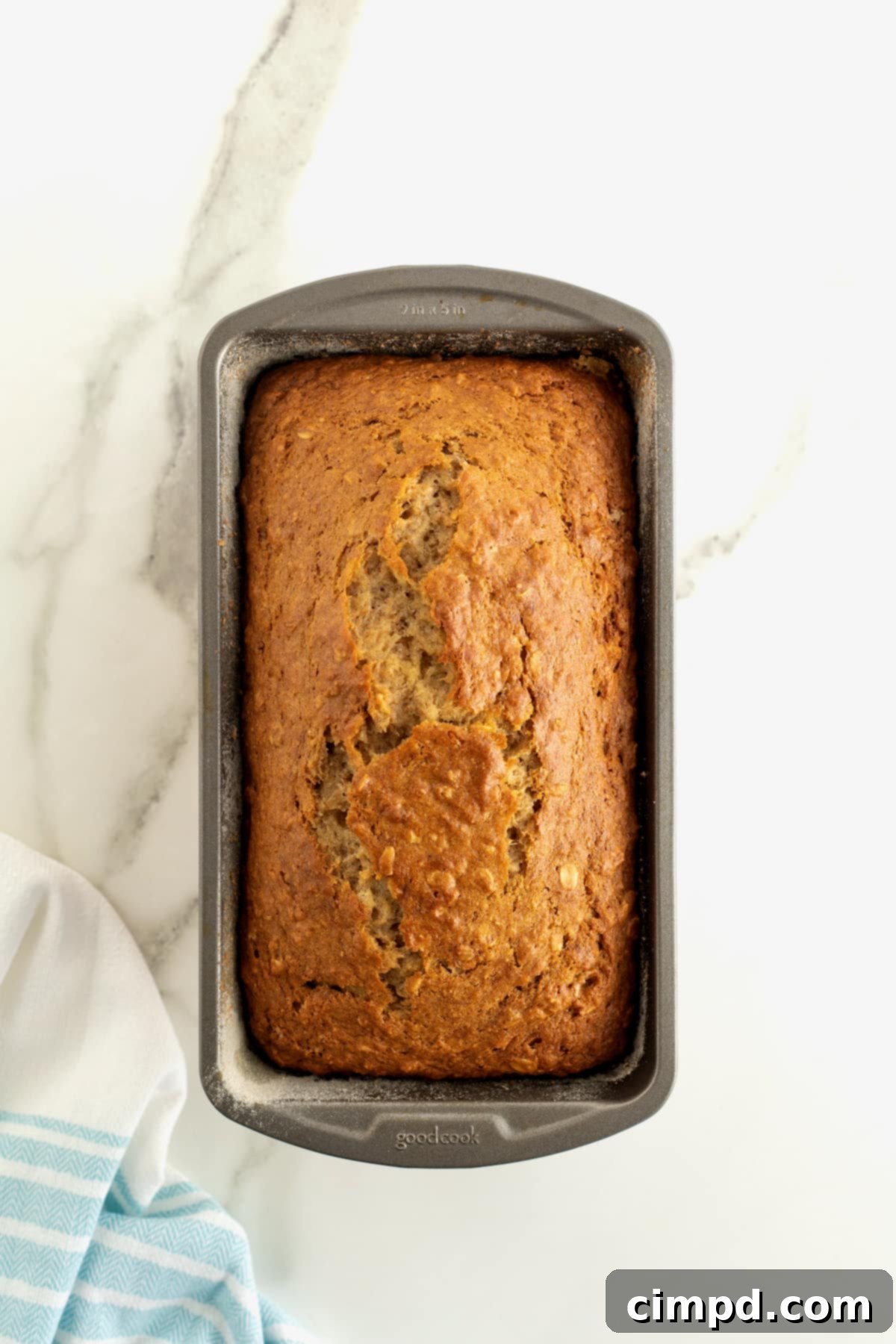 Banana Oat Whole Wheat Bread 8 A dark loaf pan of banana bread on a white marble counter.
