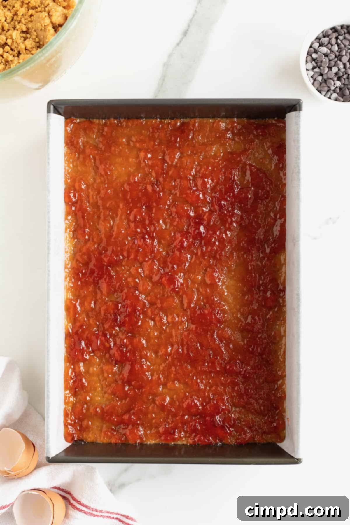 A red jelly spread over a peanut butter base in a parchment lined aluminum baking pan.
