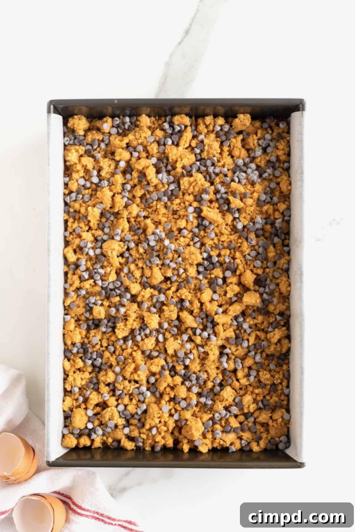 Chocolate chip streusel on top of peanut butter and jelly bars in a parchment lined aluminum baking pan.