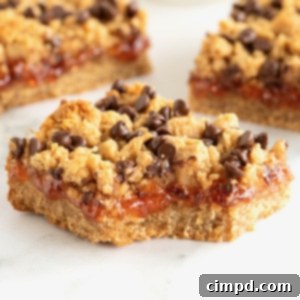 Three peanut butter and jelly bars topped with mini chocolate chips on a white surface. The front bar has a bite out of it.
