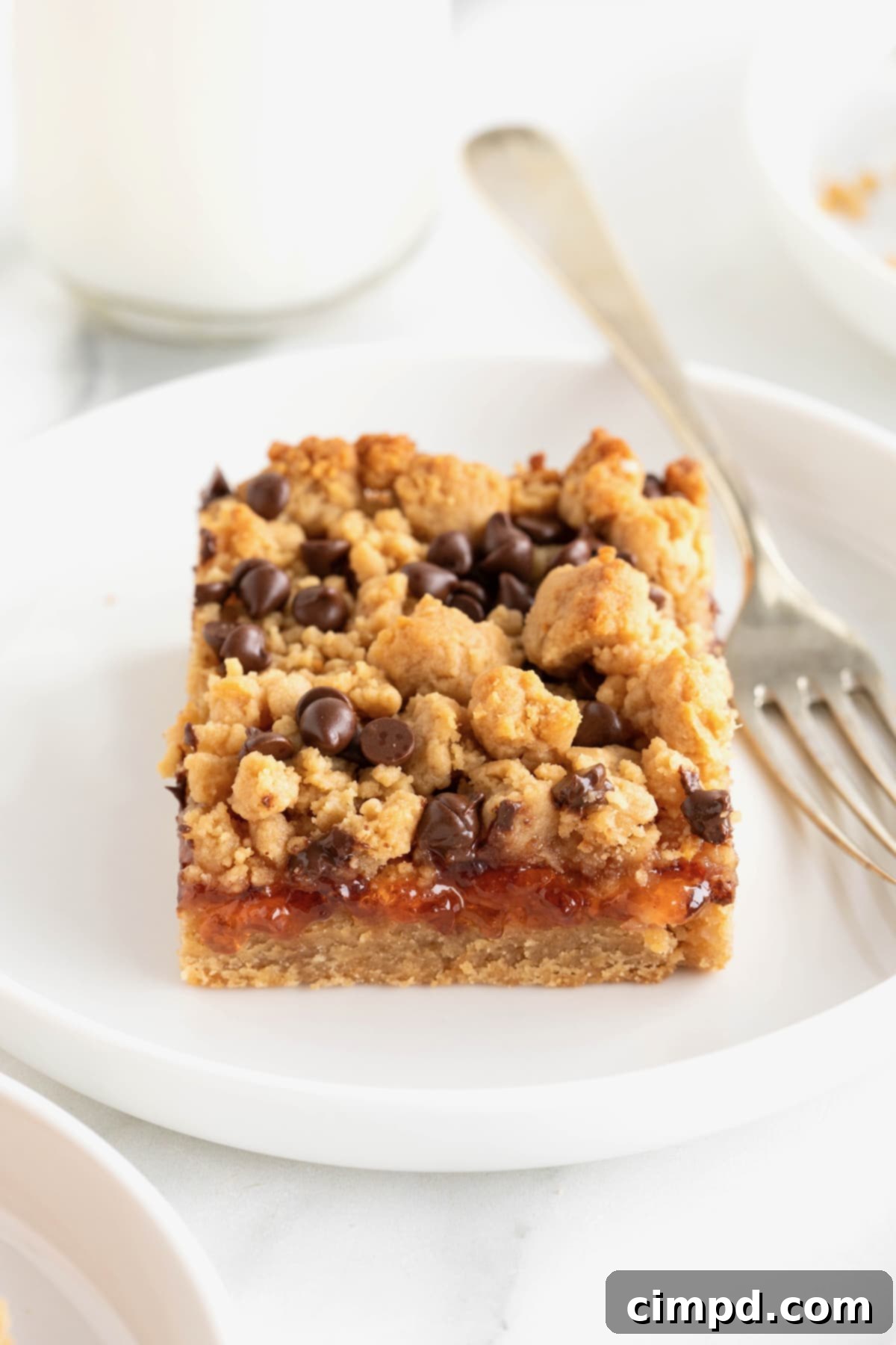 A peanut butter and jelly bar on a white plate with a fork next to it.