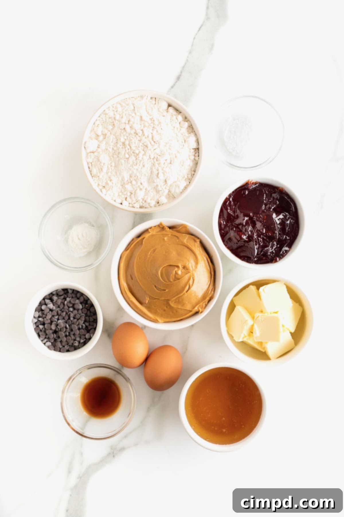 Ingredients to make peanut butter and jelly bars in small glass dishes on a white marble counter.