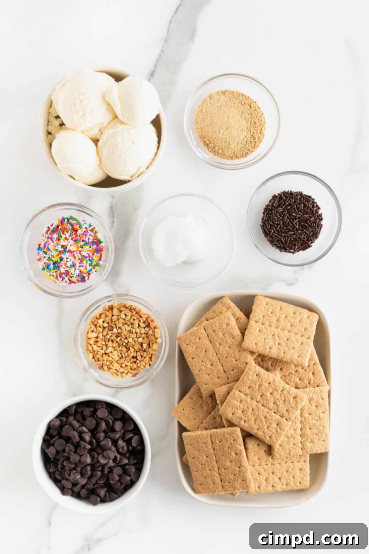 Ingredients to make graham cracker ice cream sandwiches in small glass dishes on a white marble counter.