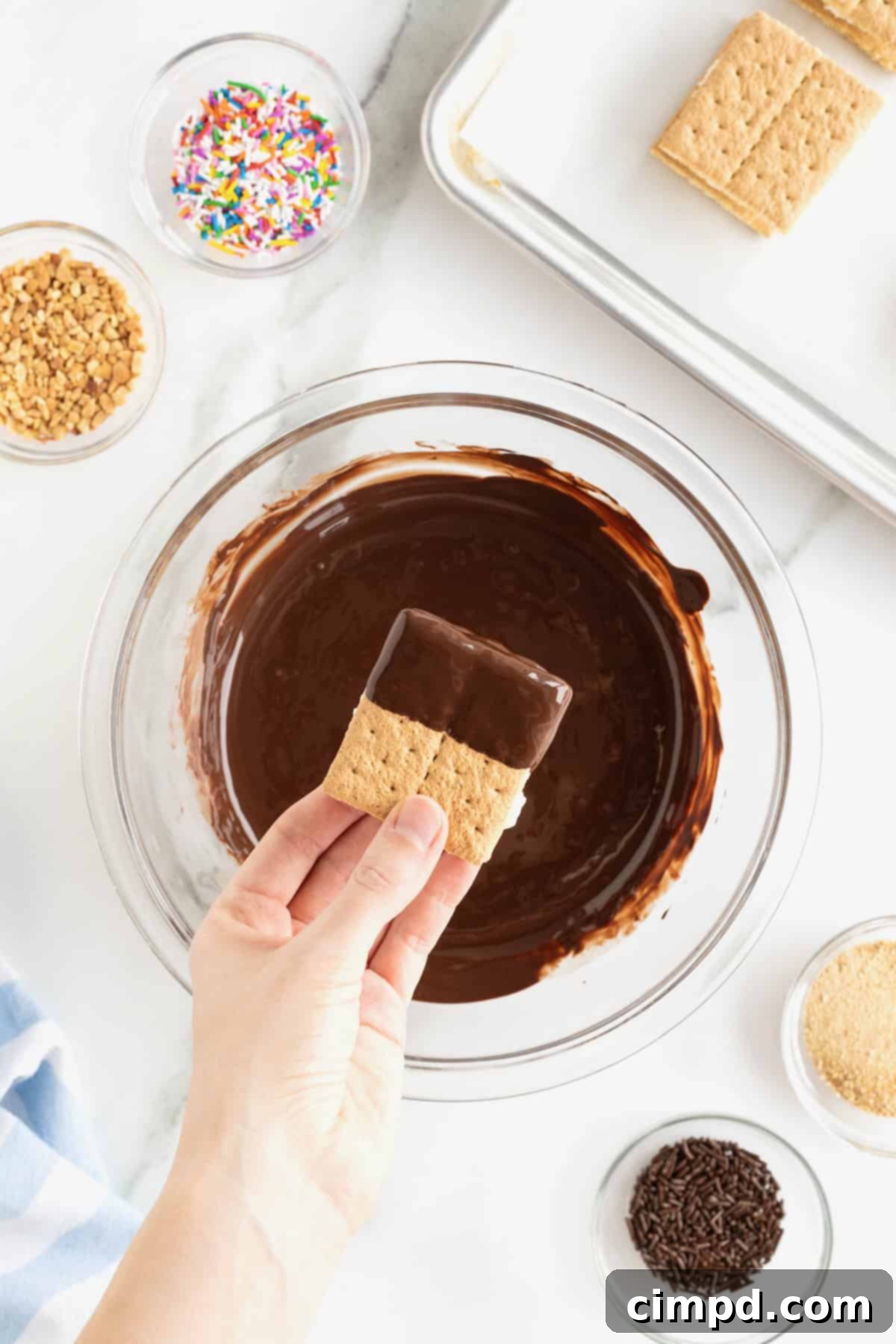 A graham cracker ice cream sandwich being dipped into melted dark chocolate in a glass bowl.