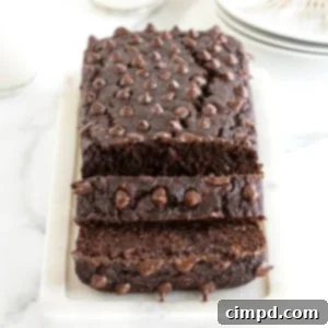 A top-down view of a delicious loaf of Flourless Chocolate Banana Bread, featuring a rich, dark brown color and studded with an abundance of melted chocolate chips, presented on a rustic square cutting board.