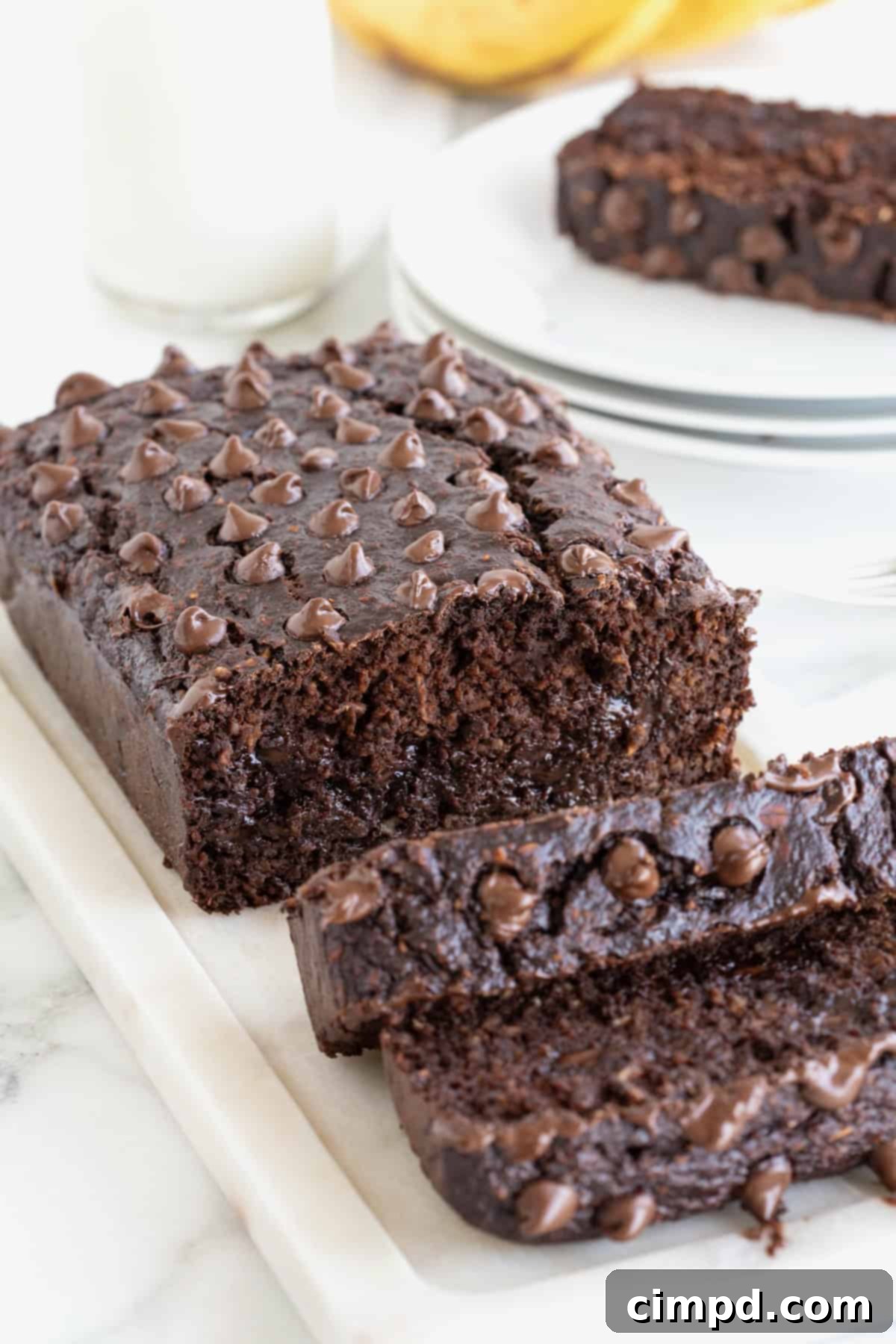 Another view of a freshly baked loaf of Flourless Chocolate Banana Bread, boasting a delightful sprinkle of chocolate chips on its golden-brown top. It's positioned on a rustic white cutting board, contrasting beautifully with a smooth white marble counter.