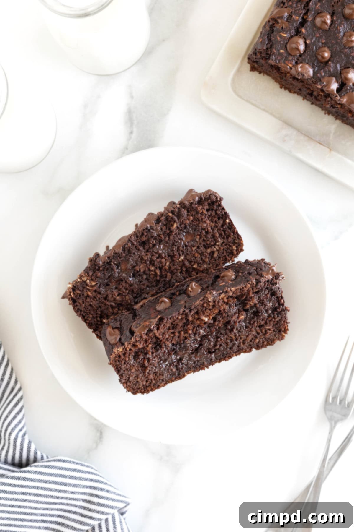 Two generous slices of warm Flourless Chocolate Banana Bread, perfectly baked and showcasing their rich chocolate interior, rest invitingly on a small white rimmed plate.