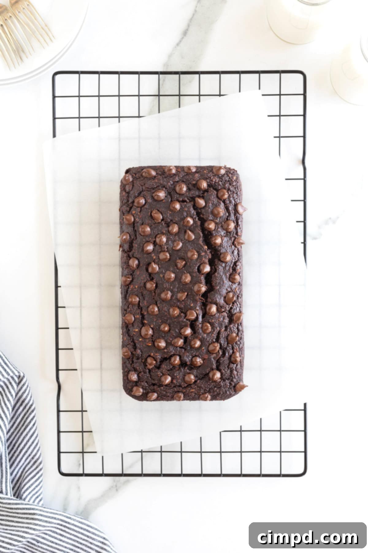 A freshly baked loaf of Flourless Chocolate Banana Bread, still warm, cooling gracefully on a parchment-lined wire rack. The dark chocolate chips dotting its surface hint at the deliciousness within.