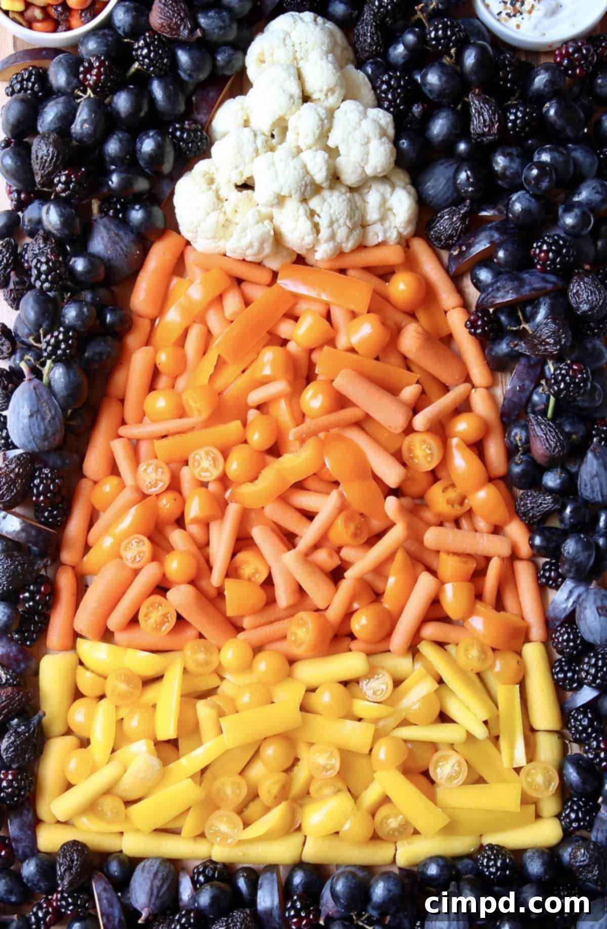Close-up of Candy Corn Snack Board ingredients: cauliflower, orange and yellow vegetables, and black fruits.