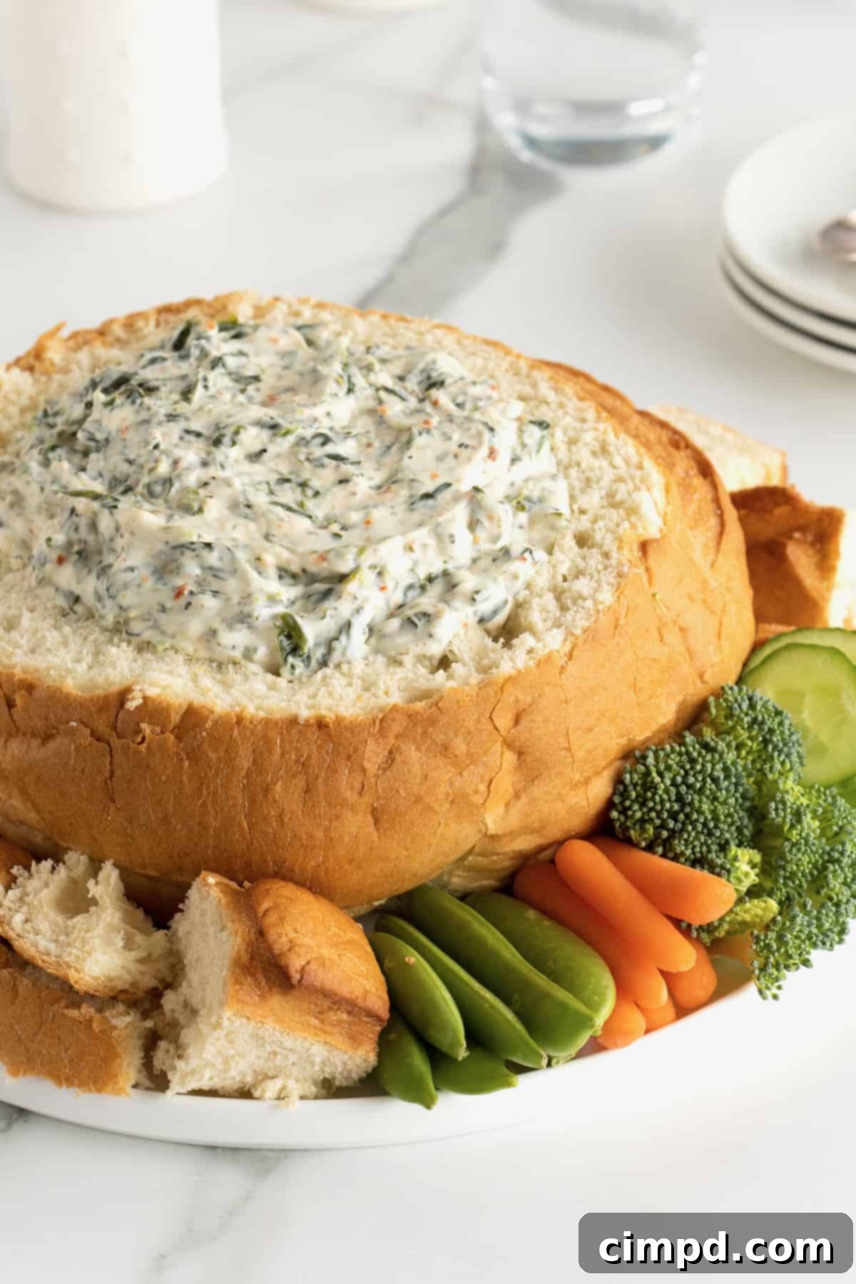 Creamy spinach dip in a bread bowl, beautifully presented with vibrant fresh vegetables and bread chunks for dipping.