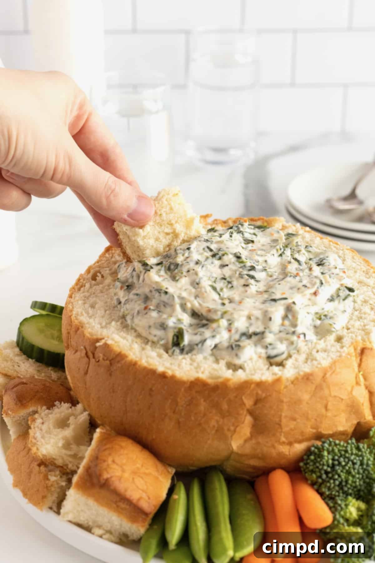 Rich and creamy spinach dip served in a rustic bread bowl, artfully surrounded by a colorful selection of fresh vegetables and bread chunks.