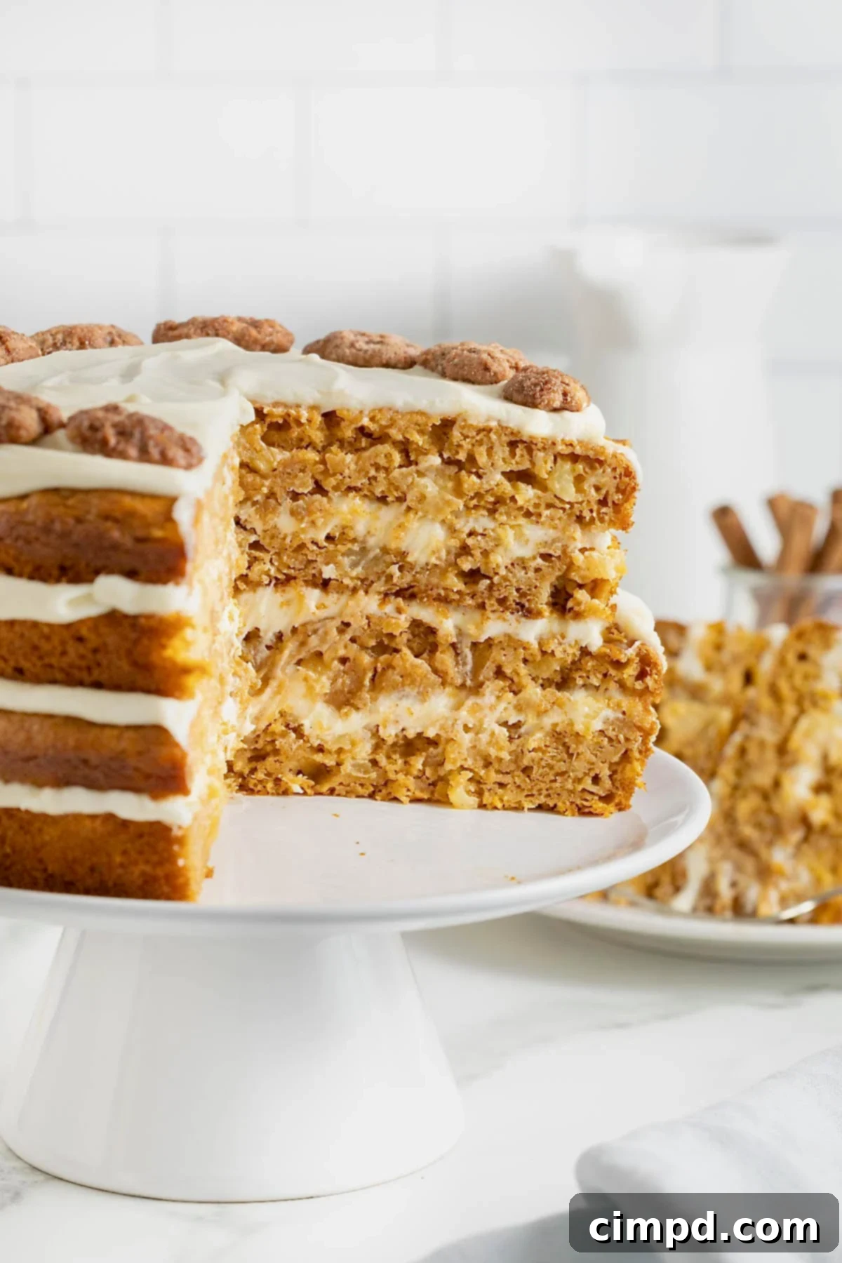 A beautifully layered pumpkin pineapple cake on a pristine white cake stand. A generous wedge has been carefully cut from the cake, revealing its moist interior and distinct layers of cake and creamy frosting.