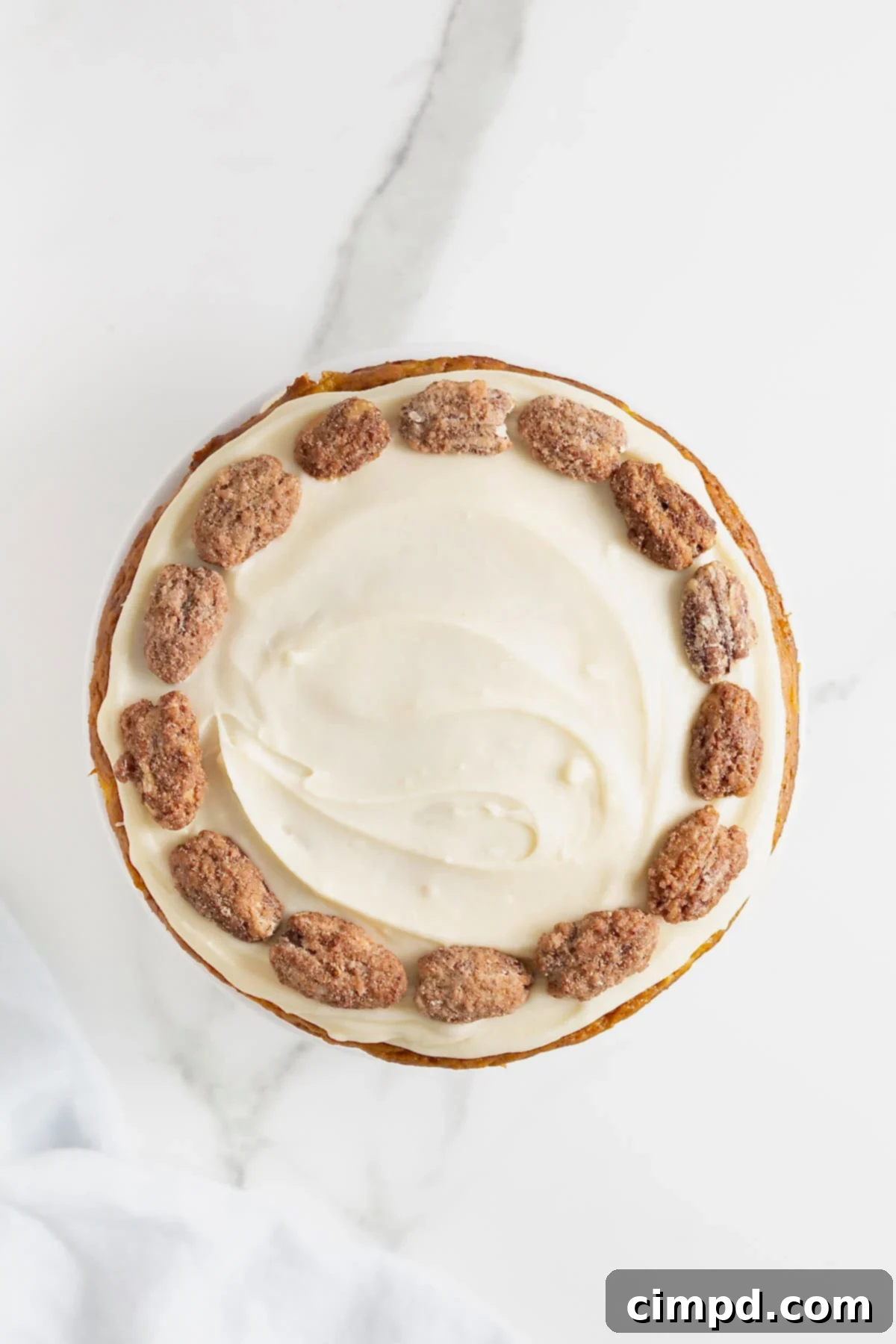 A close-up view of the top of a white frosted cake, elegantly decorated with a ring of candied pecans.