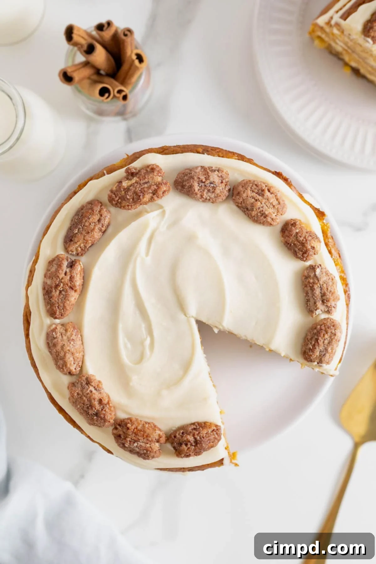 A beautiful cake with white buttercream frosting and candied pecans, viewed from above, with a single slice already removed.