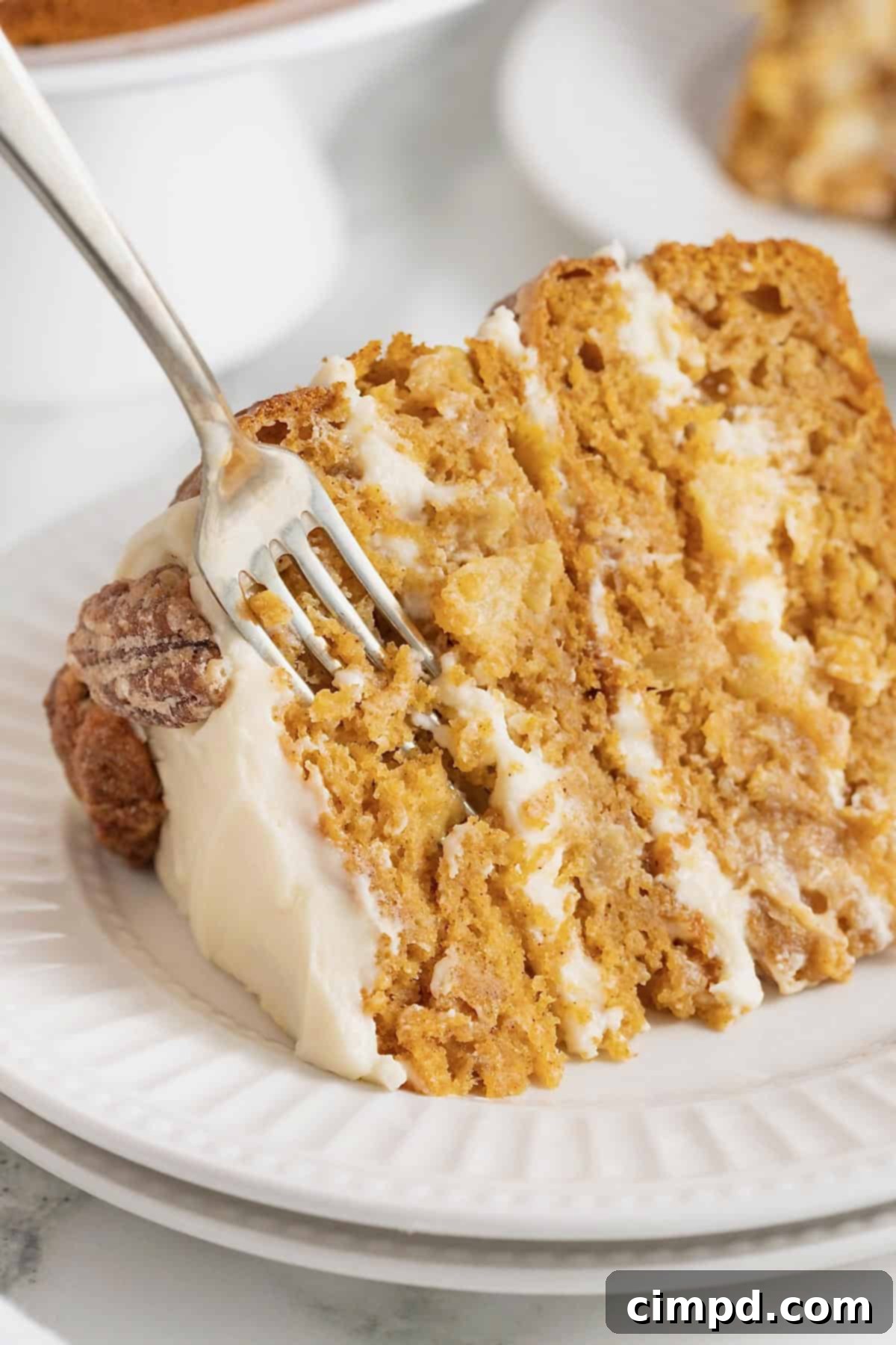 A fork piercing a delectable slice of pumpkin pineapple cake, resting on an elegant white fluted plate, highlighting its tender texture and inviting layers.