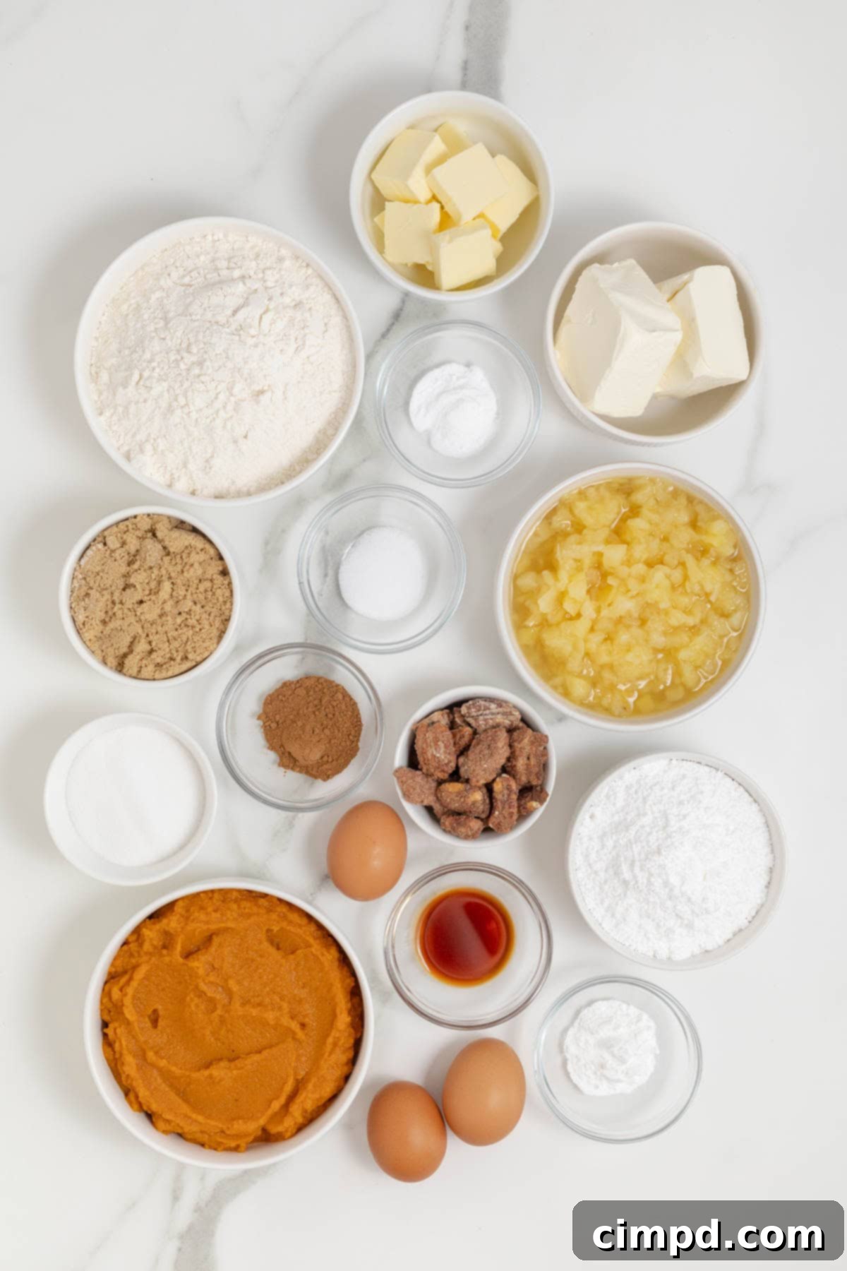 Various ingredients for pumpkin pineapple cake, neatly arranged in small glass dishes, on a white marble countertop, ready for baking.