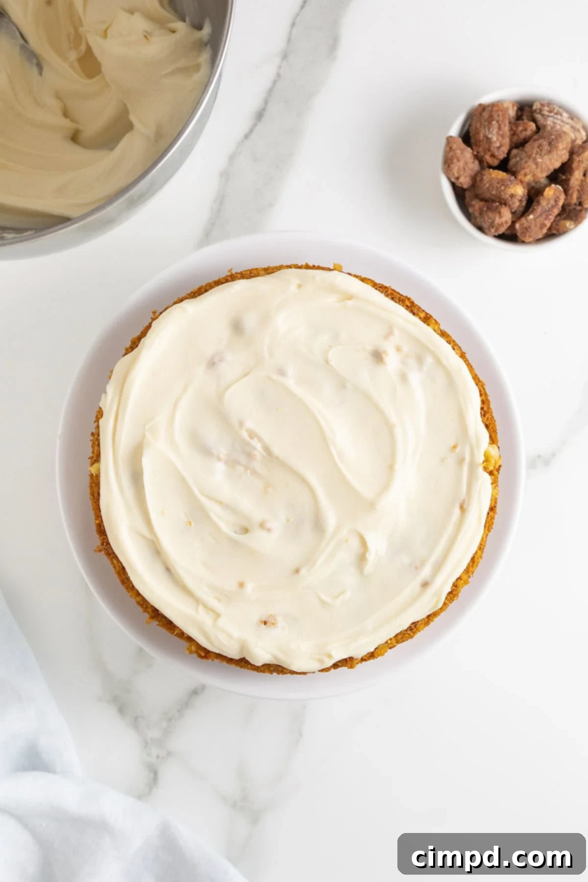 A detailed overhead shot of a round cake on a white cake stand, showcasing a freshly applied, smooth layer of white buttercream icing.