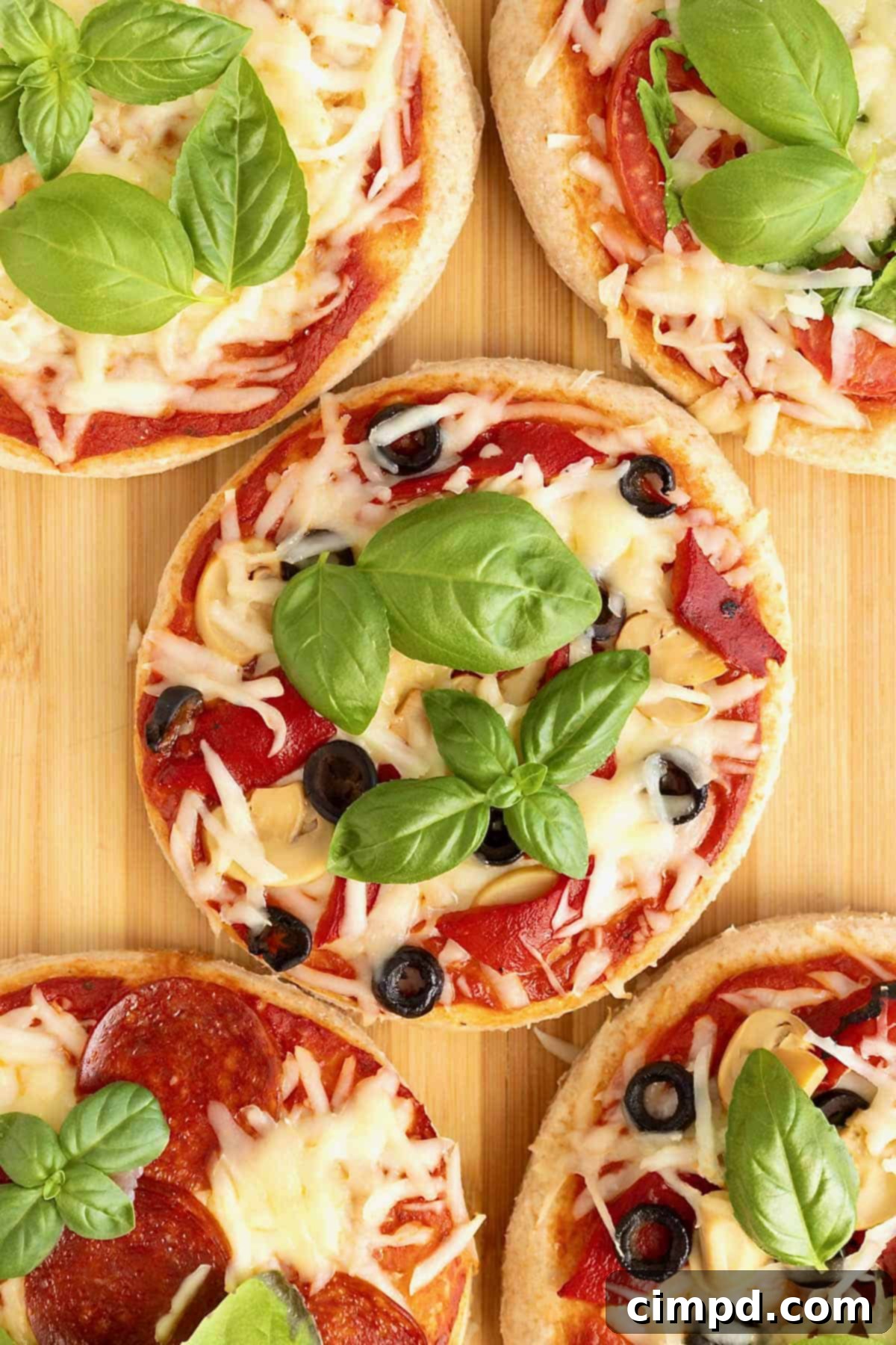 Personal size pizzas topped with shredded mozzarella, sliced black olive and fresh basil on a wooden cutting board, showcasing a healthy whole wheat Greek yogurt crust.