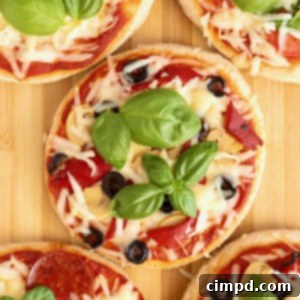 Personal size pizzas topped with shredded mozzarella, sliced black olive and fresh basil on a wooden cutting board.