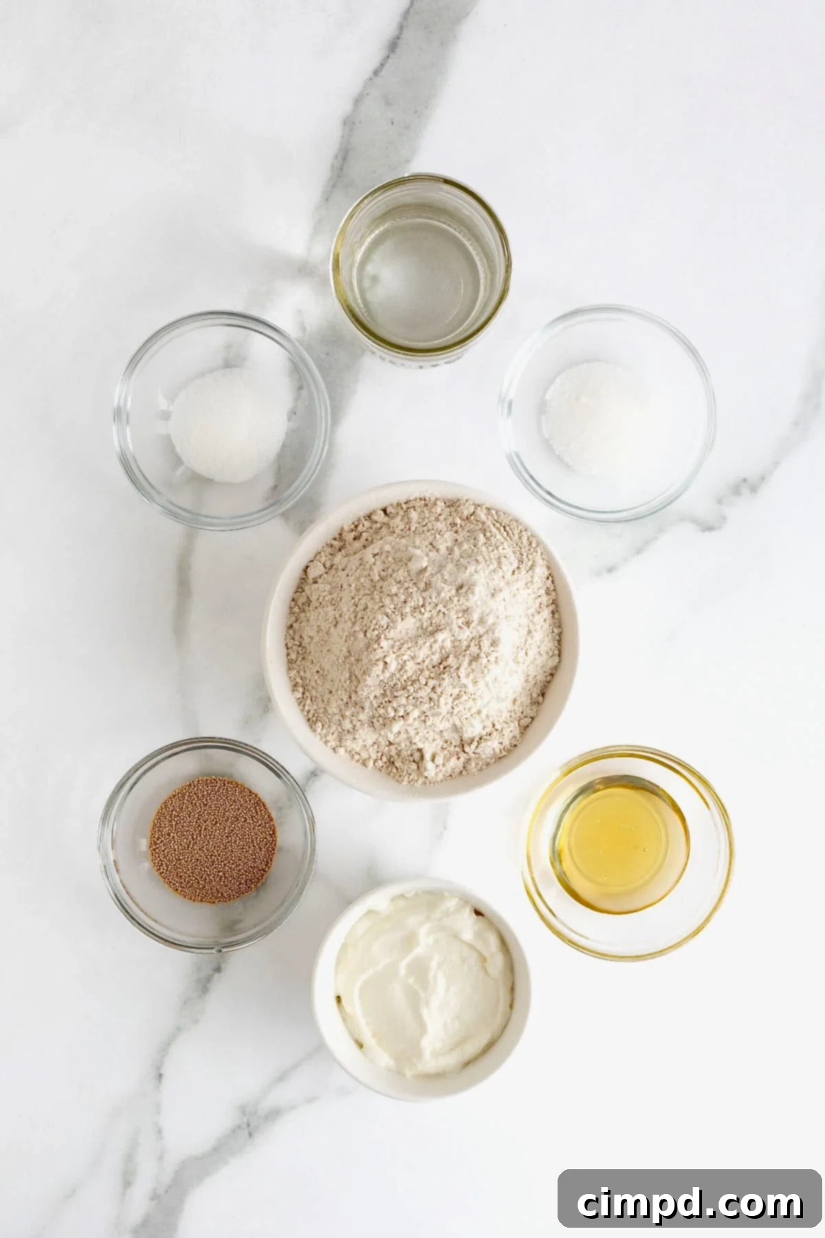 Various raw ingredients for making whole wheat greek yogurt pizza dough, including flour, yeast, honey, and Greek yogurt, arranged on a countertop.