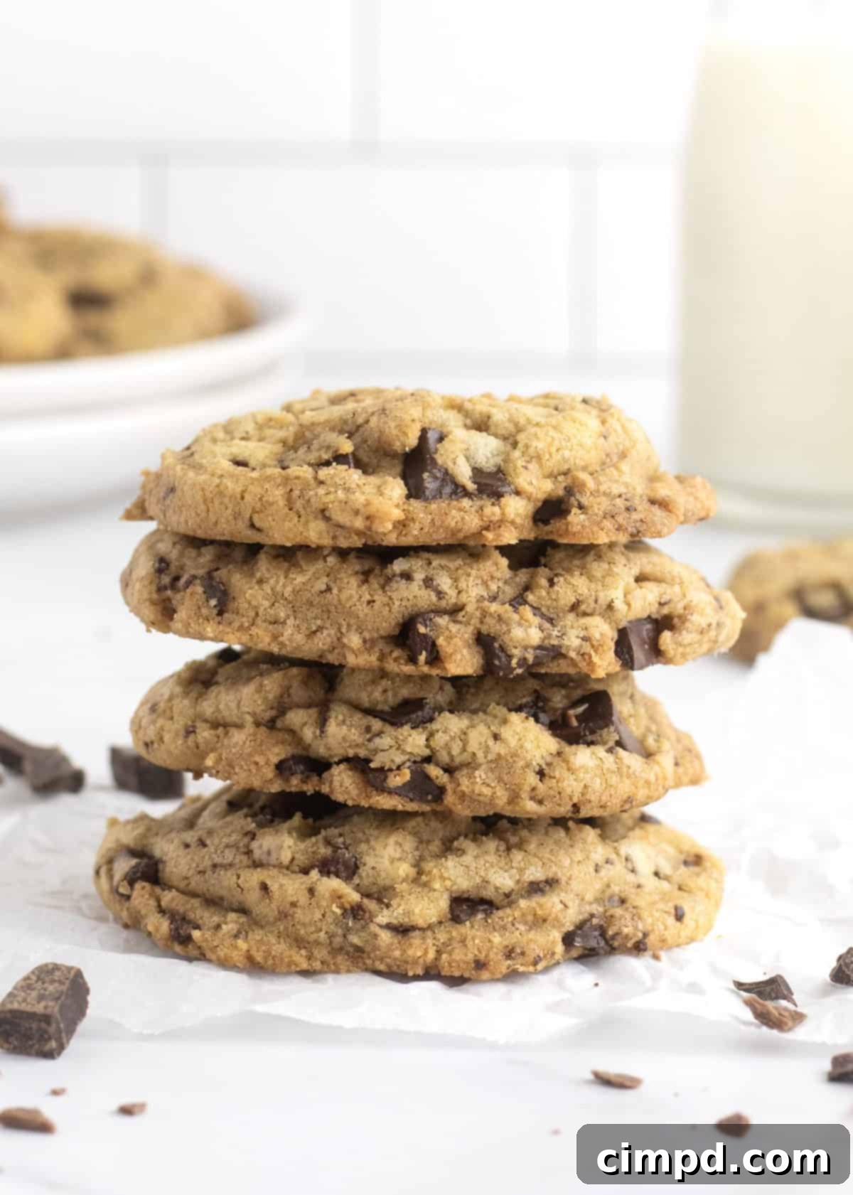 A stack of golden brown, perfectly baked chocolate chip cookies on a white plate, ready to be enjoyed.