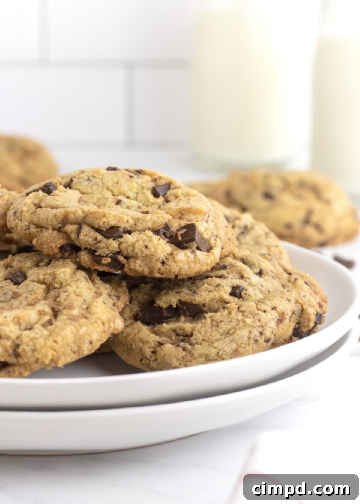 Two perfect chocolate chip cookies on a white plate with a glass of milk in the background, inviting a delicious break.