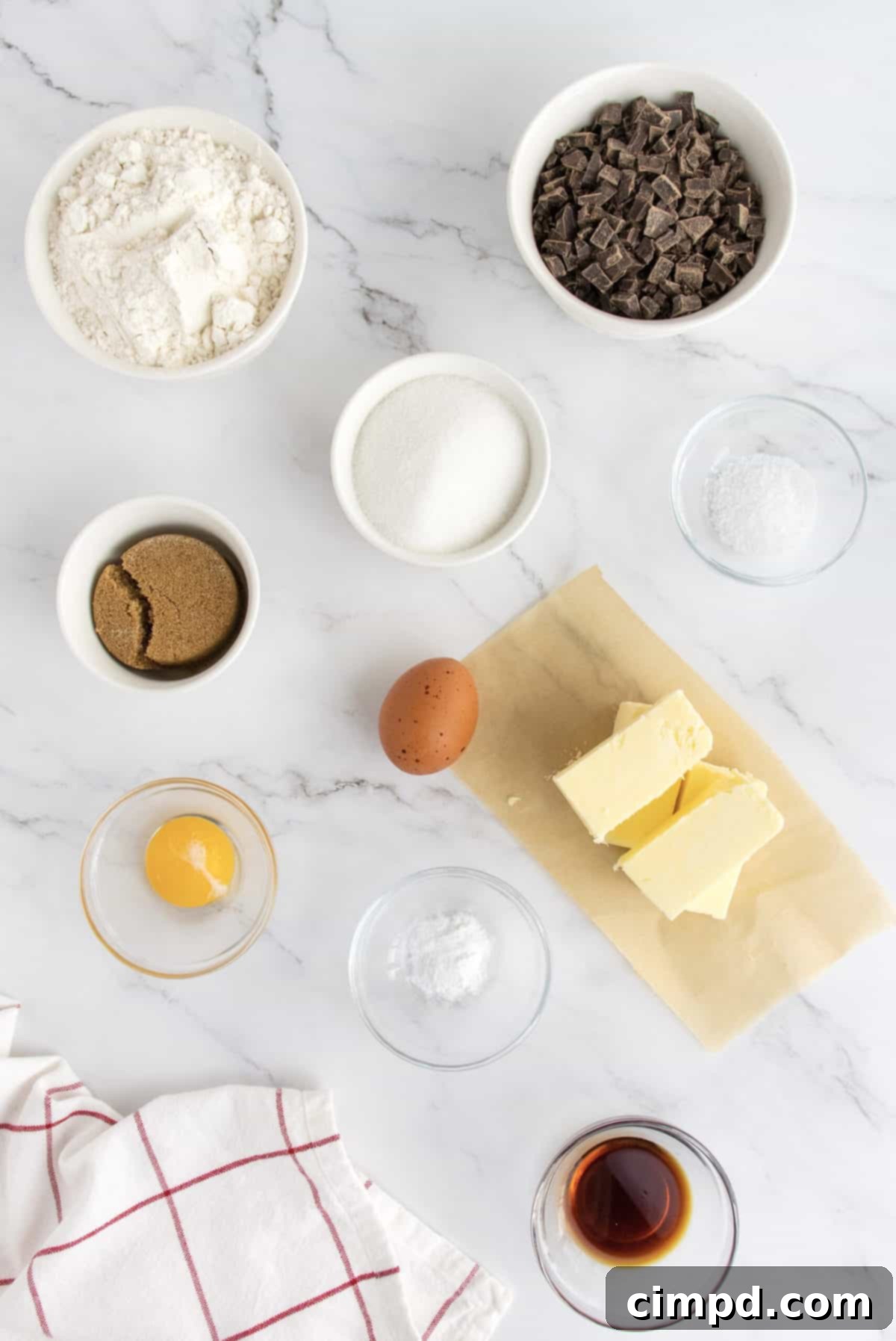 Ingredients for chocolate chip cookies laid out, including butter, eggs, flour, chocolate, and sugar.