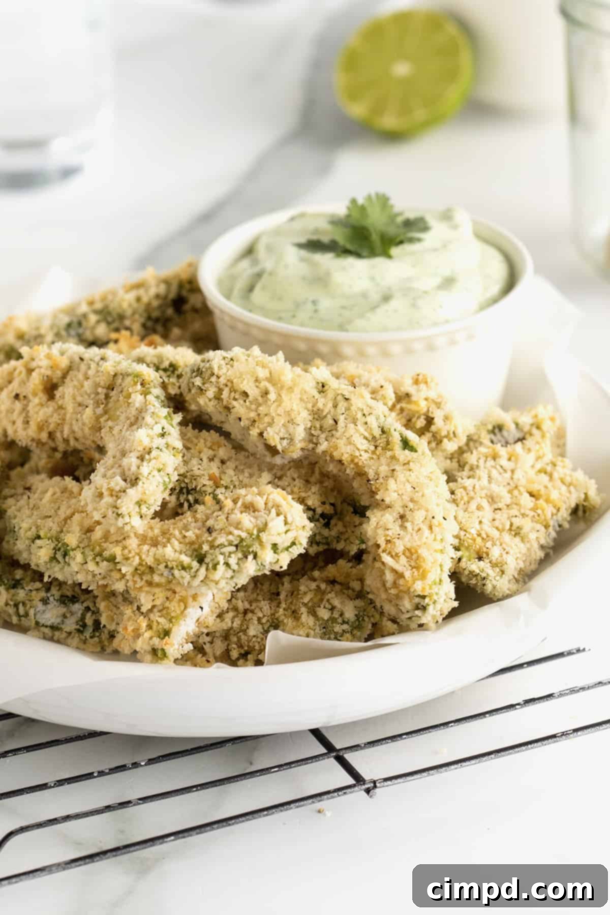 A beautifully arranged serving platter of golden brown baked avocado fries, accompanied by a small dish of vibrant cilantro lime dipping sauce, ready for enjoyment.