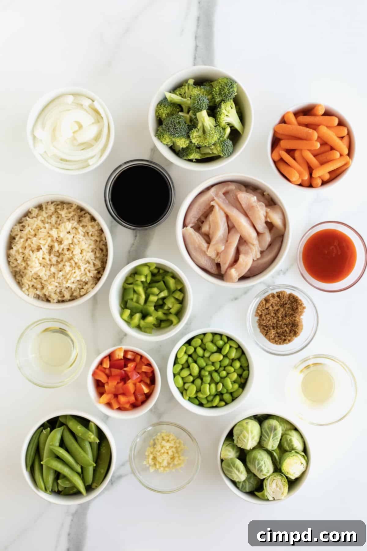 A colorful spread of fresh stir fry ingredients, including thinly sliced chicken breast, chopped bell peppers, broccoli, brussels sprouts, carrots, and edamame, ready for cooking.