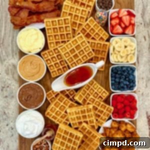 A rectangular wood food board filled with waffles, fruits, bacon and