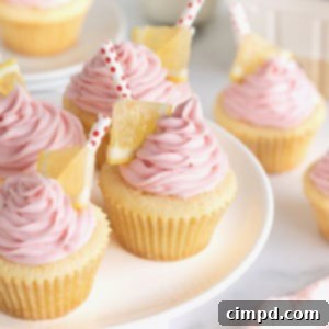A white cake stand topped with lemon cupcakes with pink frosting garnished with a small triangle of lemon and a red and white polka dot straw.