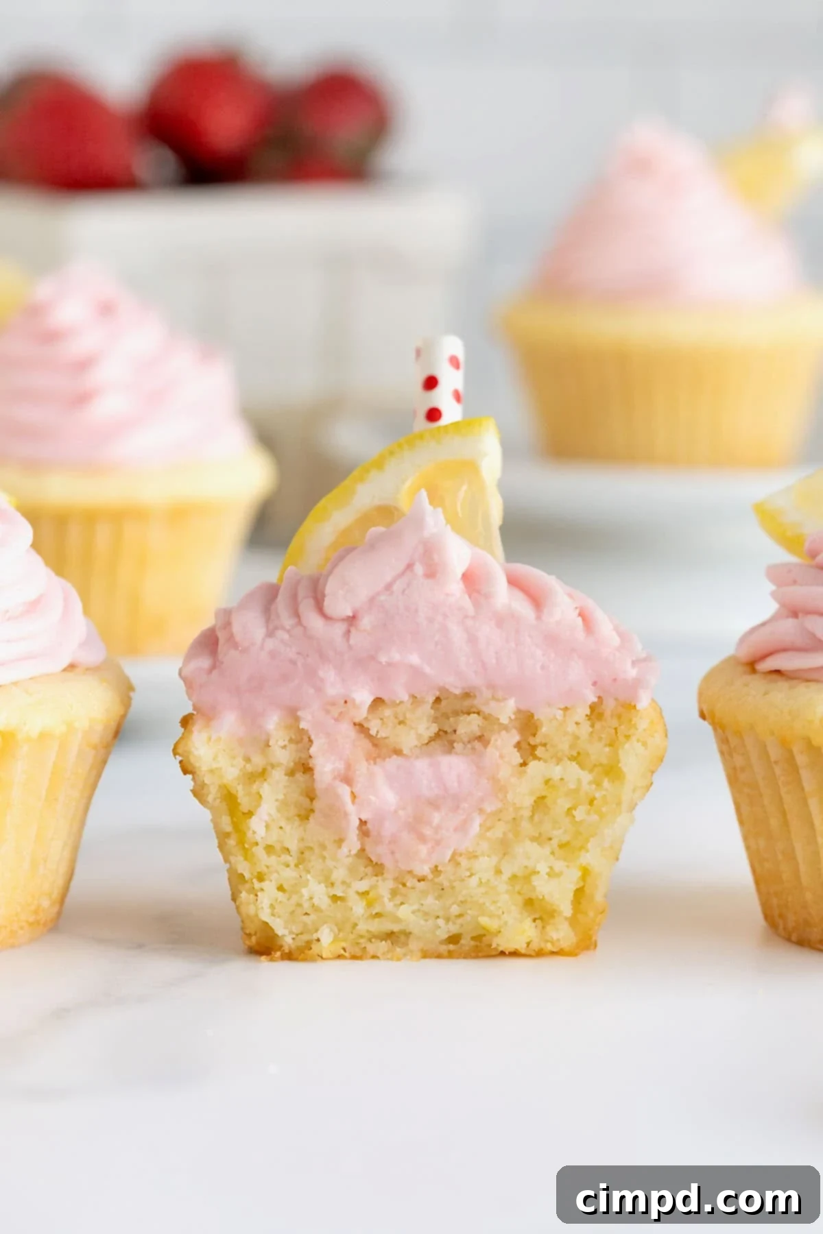 A strawberry lemonade cupcake cut in half, revealing a generous pocket of rich strawberry frosting filling.